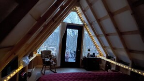 An attic bedroom with a sloped ceiling, a bed with a plaid blanket, a chair, and a small table. - Hillside: Cozy offgrid cabin near Cooperstown, NY (Cherry Valley)