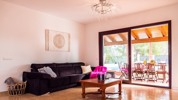Ein Wohnzimmer mit einem dunkelblauen Sofa, einem Holztisch und einer großen Schiebeglastür, die zu einem Essbereich im Freien führt.