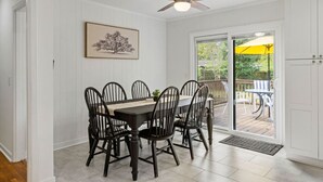 A dining area with a table and chairs, a ceiling fan, a door, and a view of an outdoor deck.