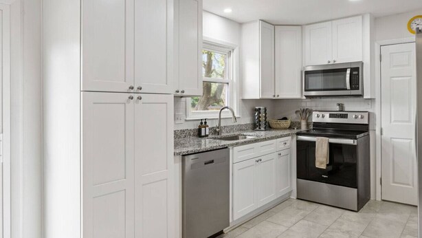 A modern kitchen with white cabinets, stainless steel appliances, and a granite countertop.