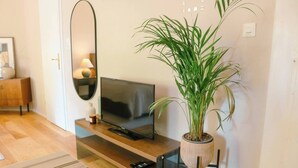 Un salon moderne avec un téléviseur à écran plat posé sur une console en bois, une plante en pot et un miroir accroché au mur.