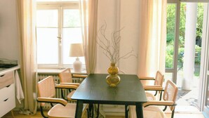 Un coin repas comprenant une table et six chaises, un vase avec des branches et une fenêtre avec des rideaux.