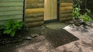 Une cabane rustique en rondins de bois, dotée d’une porte en bois et d’un petit porche.
