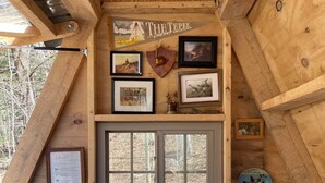 Une chambre mansardée chaleureuse, avec un plafond en pente en bois, une grande fenêtre et un lit recouvert d’une couverture à carreaux.