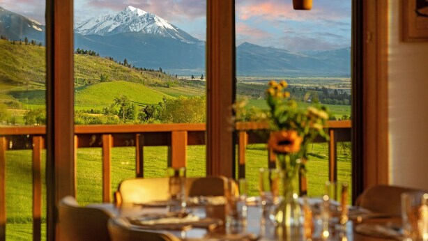 A dining table set with glasses and a vase of flowers, overlooking a mountainous landscape through large windows. - Spacious home with mountain and valley views, seconds to Deep Creek trailhead (Livingston)