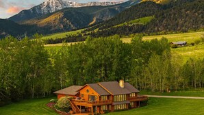 A large wooden cabin with a deck, surrounded by a well-maintained lawn and dense forest, with mountains in the background. - Spacious home with mountain and valley views, seconds to Deep Creek trailhead (Livingston)