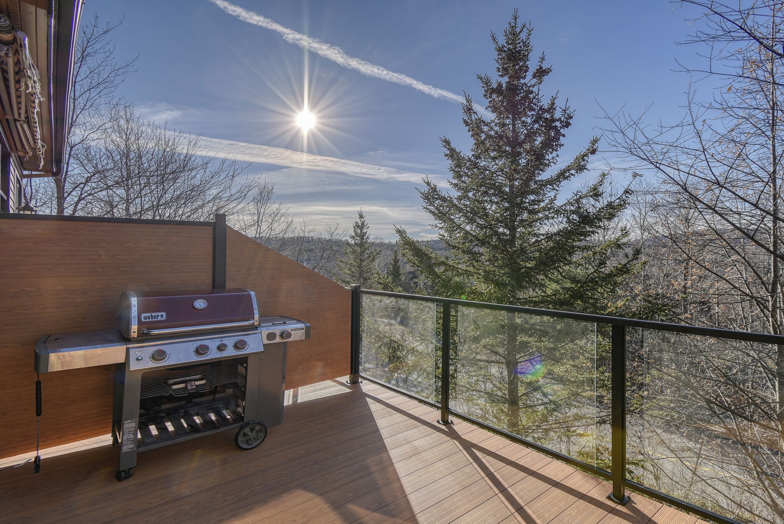 A wooden deck with a portable grill, overlooking a forested area.