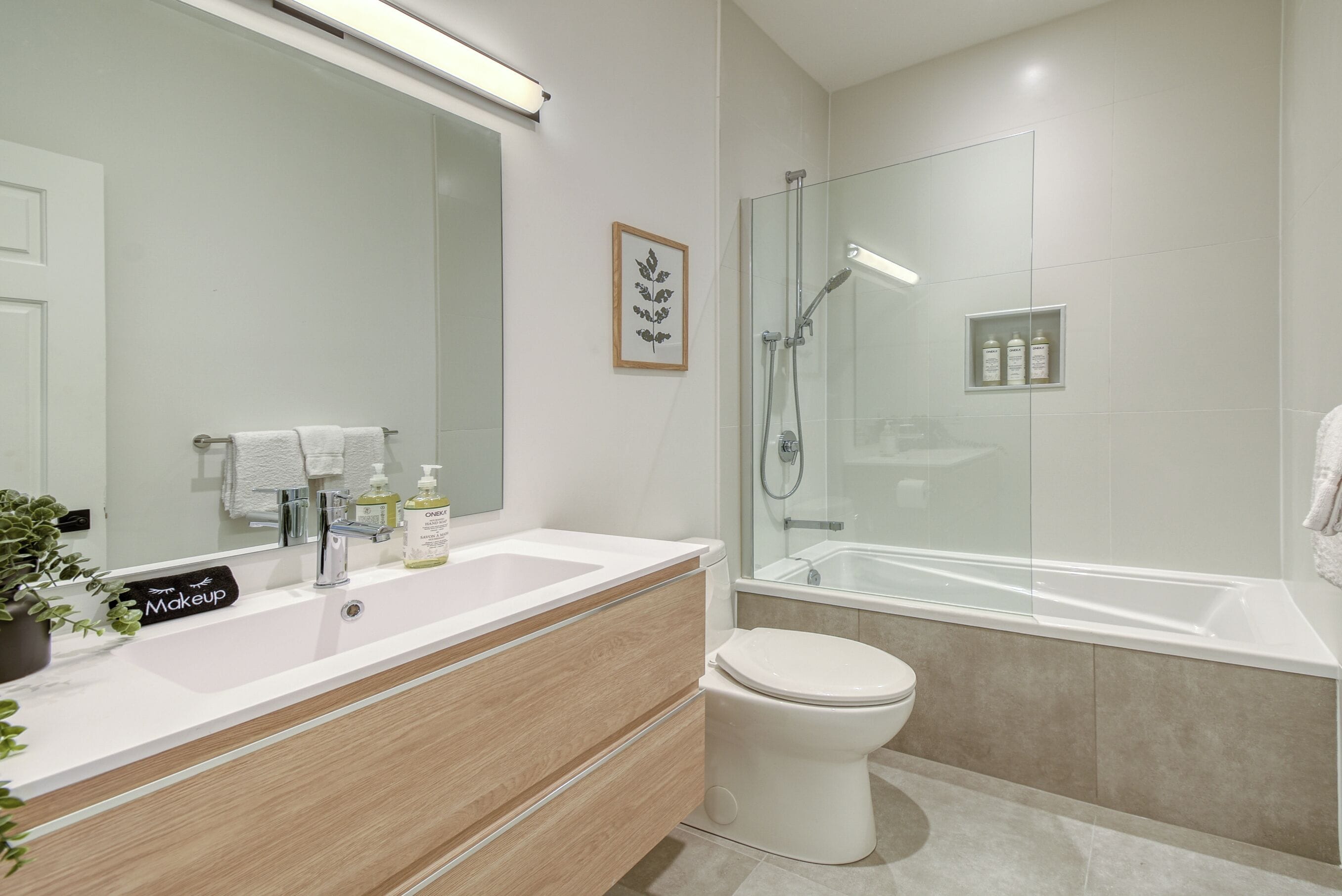 Ein modernes Badezimmer mit Waschbecken, Waschtisch und Toilette. Es beinhaltet einen Duschbereich mit Glasabtrennung und eine Badewanne.