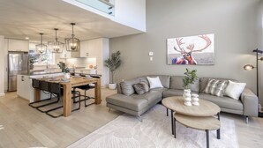 Uma cozinha moderna com área de refeições, uma sala de estar com sofá e mesa de centro, e um quadro grande de um veado na parede.