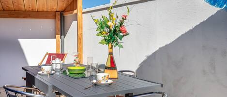 A table set outdoors with chairs, a vase of flowers, and a wooden pergola overhead.