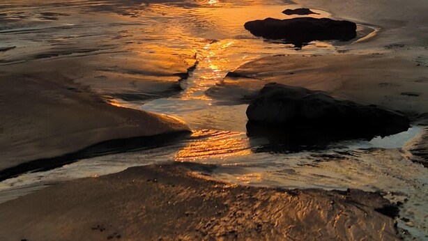 Tramonto su una spiaggia con acque calme che riflettono il cielo.