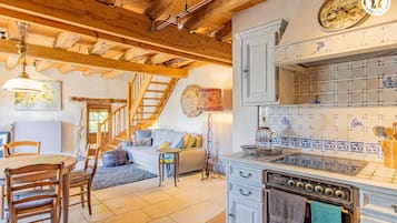 Une cuisine rustique avec des poutres en bois, un coin repas avec une table et des chaises, et un escalier menant à un autre niveau.