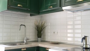 Una cocina con armarios verdes, un lavamanos de acero inoxidable, una planta en maceta y una tetera sobre la encimera.