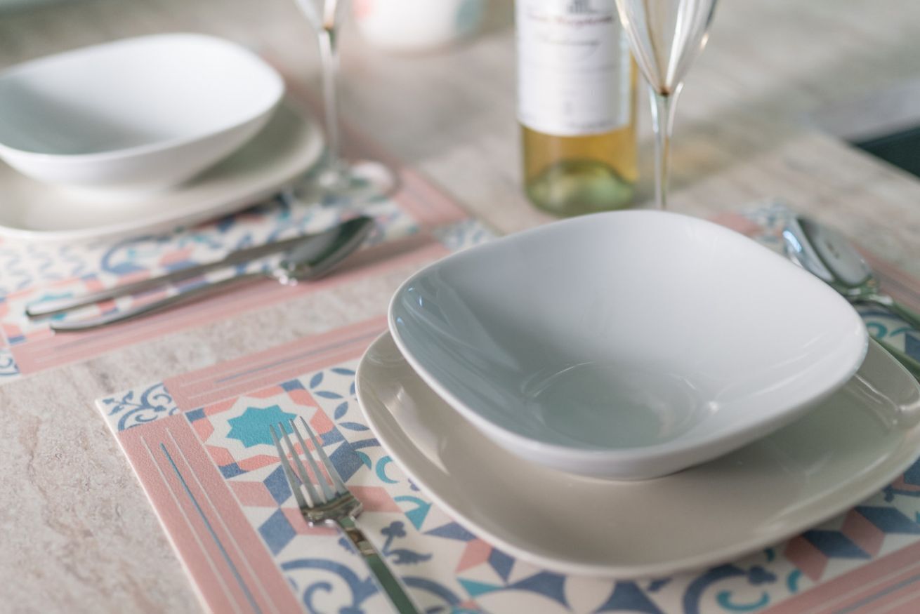 Una mesa dispuesta con platos, cubiertos y una botella de vino.