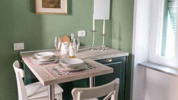 Un comedor con una mesa dispuesta para dos personas, un cuadro en la pared y una ventana con persianas.