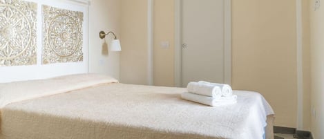 A neatly made bed with a white bedspread and a folded towel on the side.