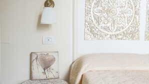 Un dormitorio con una cama, una lámpara de pared, un panel decorativo y una mesita con tablero estampado.