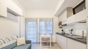 A compact kitchen with a dining table, a sofa, and a window with sheer curtains.