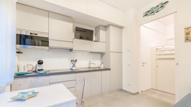 A modern kitchen with white cabinetry, a built-in oven, and a dining area with a white table and chairs.