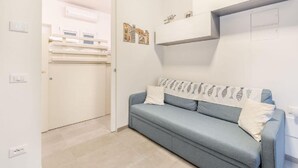 A room with a light blue sofa, a white door, and a wall-mounted shelf with decorative items.