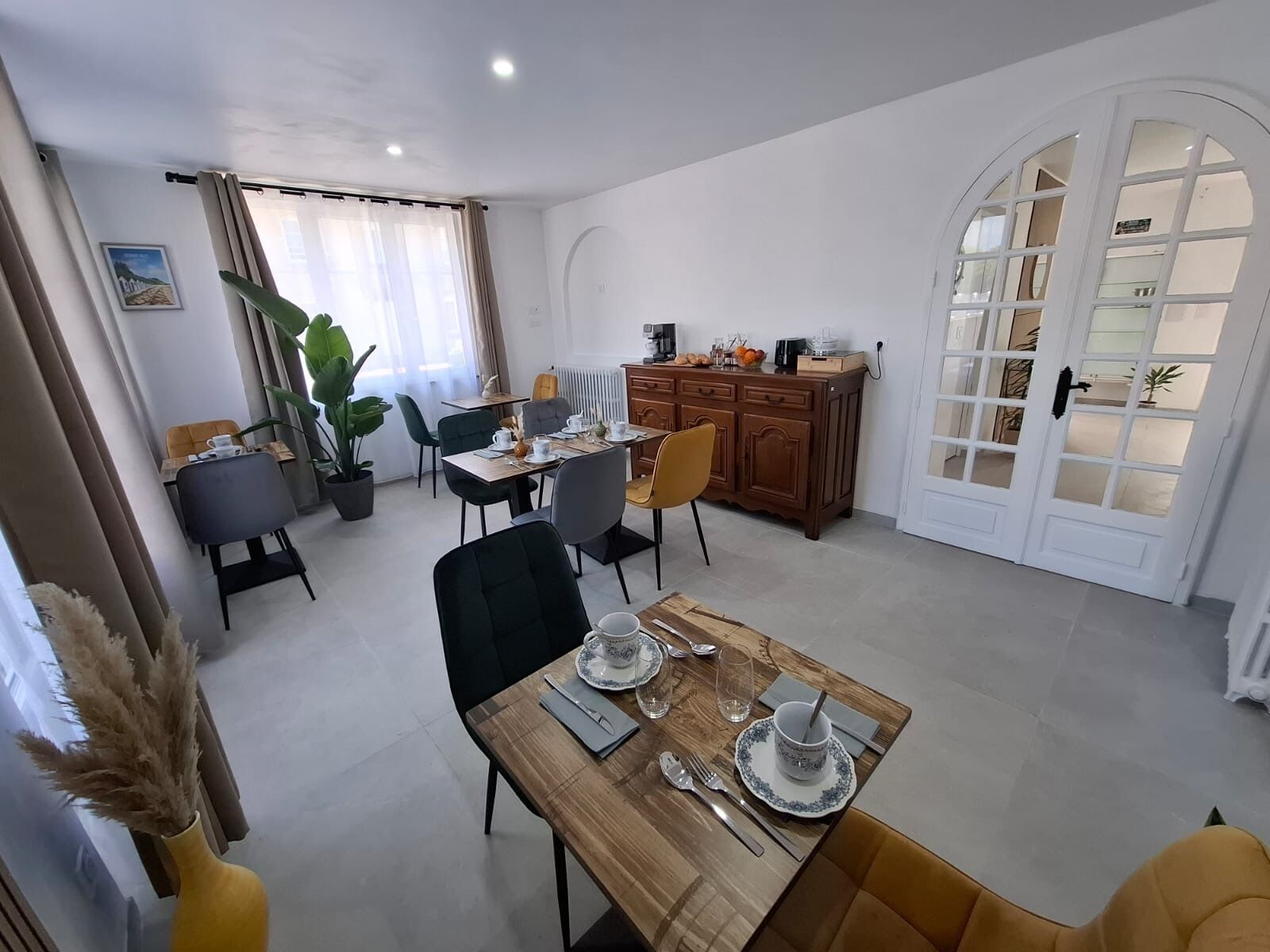 Een eethoek met een houten tafel gedekt voor vier personen, omringd door stoelen, een koffieapparaat en een kast met diverse spullen.