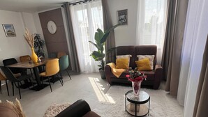 A modern living room with a brown sofa, yellow cushions, a dining area with a table and chairs, and a large window with curtains. - Luxury detached house (Montebourg)