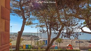 A view of a beach with a building in the foreground, a blue door, and a small structure with a red roof. - Music of the Sea- Monterosso (Monterosso al Mare)
