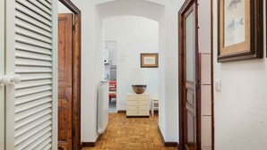 A narrow hallway with wooden flooring, white walls, and wooden doors. There is a white cabinet with drawers and a large vase on top. - Music of the Sea- Monterosso (Monterosso al Mare)