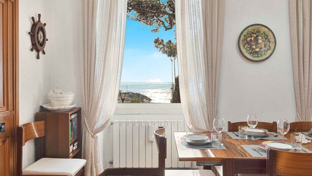 A dining room with a view of the sea, a wooden chair, a table set for two, and a ship's wheel on the wall. - Music of the Sea- Monterosso (Monterosso al Mare)