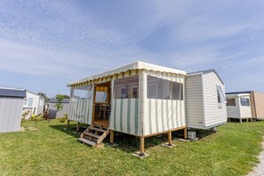 A small, single-story mobile home with a porch and a small deck, surrounded by other similar structures. - Mobile Home for 6 Guests with Shared Pool, Private Terrace, and Wi-Fi (Ambon)