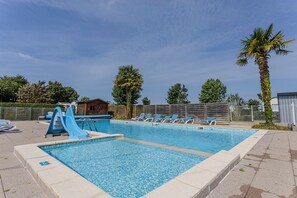 A rectangular swimming pool with a blue slide, surrounded by lounge chairs and palm trees.