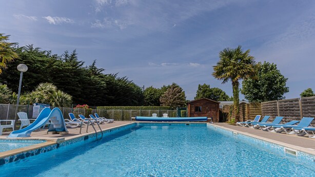 Une piscine avec des toboggans, des chaises longues et un petit bâtiment en arrière-plan.