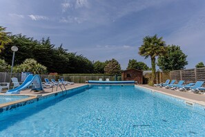 A swimming pool with slides, lounge chairs, and a small building in the background.