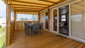 Un patio couvert avec une terrasse en bois, une table et des chaises, et une porte-fenêtre coulissante donnant sur un espace intérieur.