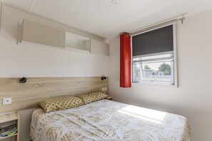 A bedroom with a bed, a headboard, a shelf, a window with a curtain, and a view outside. - Mobile Home for 6 Guests with Shared Pool, Private Terrace, and Wi-Fi (Ambon)