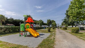 Une aire de jeux avec un toboggan et des structures d’escalade, entourée d’un chemin de gravier et de verdure.