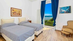 Una camera da letto con due letti, una sedia e vista sul mare.