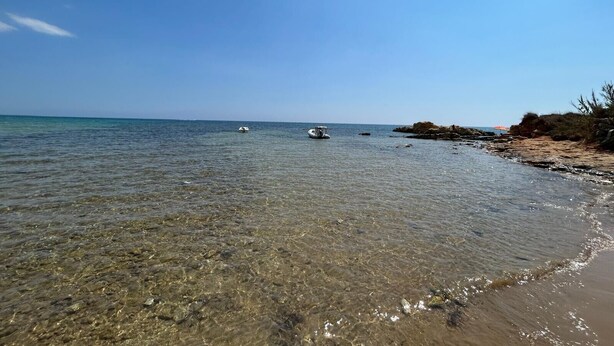 A beach with clear shallow water, a boat, and rocky terrain. - Villa 'Primavera' with sea view, private terrace and air conditioning (Marina di Modica)