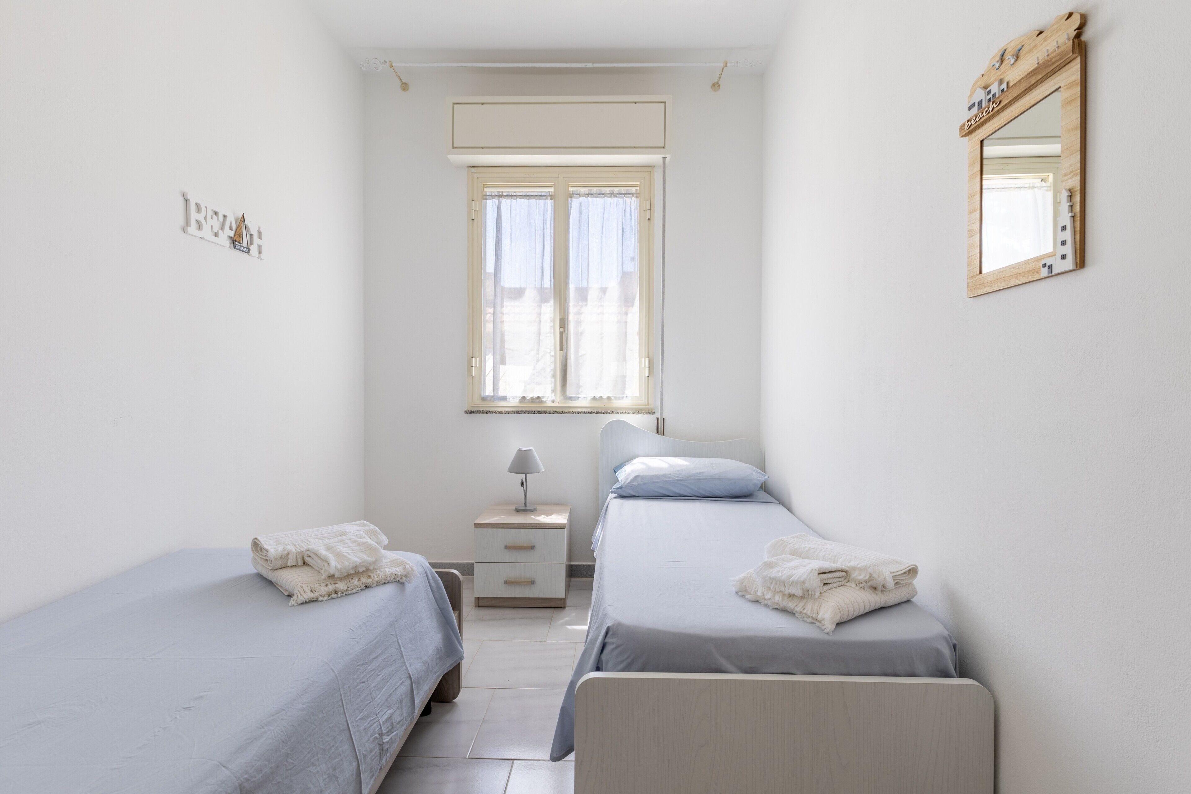 Une chambre avec deux lits, une fenêtre, une table de chevet et un miroir.