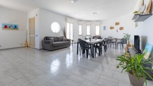 A spacious living area with a sofa, dining table, chairs, and a TV. - Villa 'Primavera' with sea view, private terrace and air conditioning (Marina di Modica)