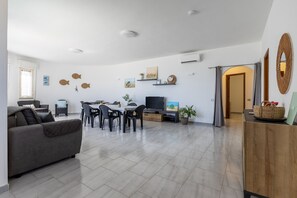 Een ruime woonkamer met een bank, eettafel, stoelen, een flatscreen televisie en decoratieve wandkunst.