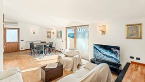 Un vaste espace de vie comprenant une table à manger, des chaises, un canapé, un téléviseur et une grande fenêtre offrant une vue dégagée.