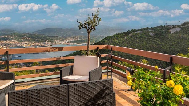 Une terrasse dotée de meubles en osier, d’une balustrade et offrant une vue sur la ville et les montagnes.