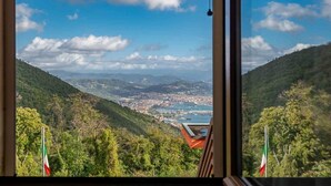 Une vue depuis une fenêtre donnant sur une ville côtière, avec des collines, un drapeau et un ciel dégagé.