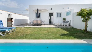 Une piscine avec une pelouse, un barbecue et une terrasse équipée de chaises et de tables.