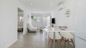 Una cocina moderna con armarios blancos, un comedor con mesa y sillas blancas, y una sala de estar con sofá blanco y una planta.