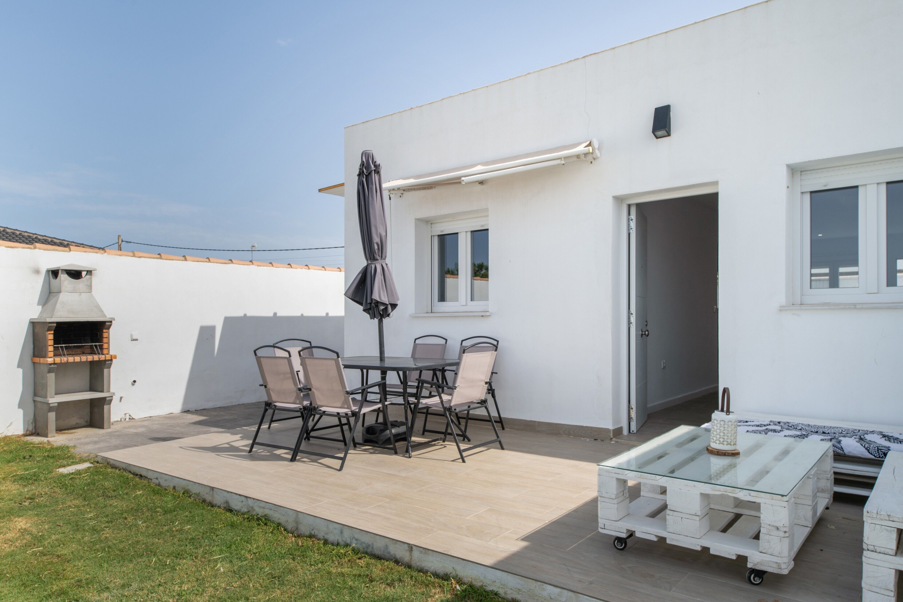 A patio with a table and chairs, a barbecue grill, and a white wall with windows.