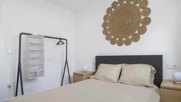 Un dormitorio con una cama, un estante en la pared, una mesita de noche con una lámpara y un adorno en la pared.