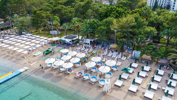 Vue aérienne d’un complexe hôtelier situé en bord de mer, avec de nombreux espaces de détente, des parasols et des chaises de plage.