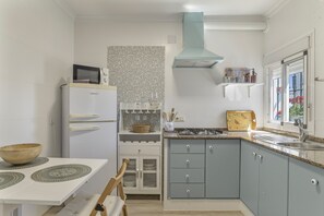 A compact kitchen with a microwave, stove, and sink, featuring a patterned backsplash and light blue cabinets.